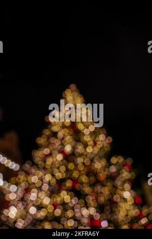Blurry Gold and red bokeh of Christmas light on Christmas tree on black background. Colourful Glitter bokeh from blurry decoration bulbs. Stock Photo