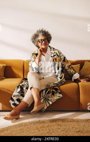 Pensive businesswoman looking away with a smile while sitting on a couch in an office lobby. Thoughtful businesswoman working in a creative coworking Stock Photo