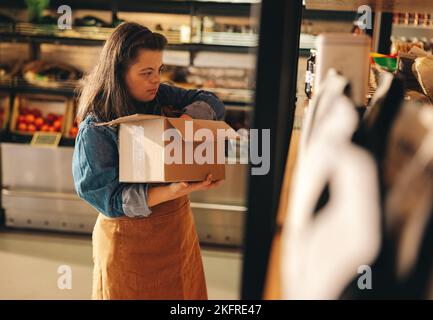 Grocery store employee with Down syndrome restocking food products onto the shop shelves. Empowered woman with an intellectual disability working as a Stock Photo