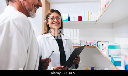Two pharmacists doing a stock take using a tablet in a drug store. Happy healthcare professionals working together in a pharmacy. Stock Photo