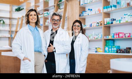 Three pharmacists standing together and looking at the camera in a drug store. Group of healthcare professionals working in a pharmacy. Stock Photo