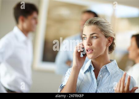 Ill have to get back to you on that. a young businesswoman talking on the phone while her colleagues stand in the background. Stock Photo