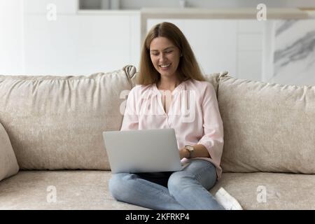 Smiling attractive woman sitting on sofa using laptop Stock Photo