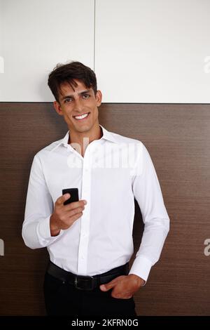 Its always nice to get feedback from clients. Portrait of a handsome young businessman standing indoors with his mobile phone. Stock Photo