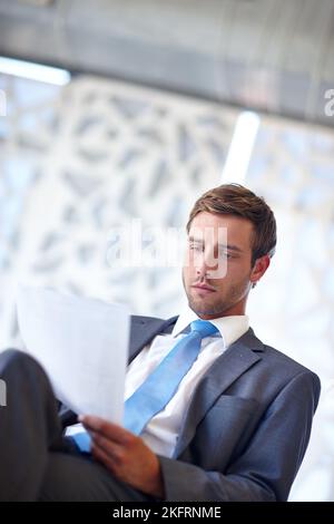 This is some serious business. a handsome young businessman reading a document in the office. Stock Photo