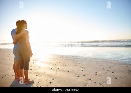 We make the most of our quiet time. a young couple looking out over the ocean on a beach at sunrise. Stock Photo
