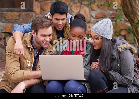 Using technology to further their education. a group of university students using a laptop while sitting on campus. Stock Photo