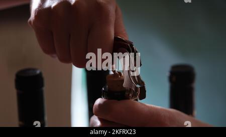 Opening of wine bottle over dark background with two bottles. Stock Photo