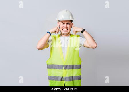 Young engineer covering his ears isolated, Builder man with ear pain, Concept of engineer covering his ears with pain expression, Engineer with ear pa Stock Photo