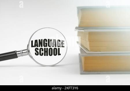 Education concept. On a white background, books and a magnifying glass, inside which it is written - language school Stock Photo