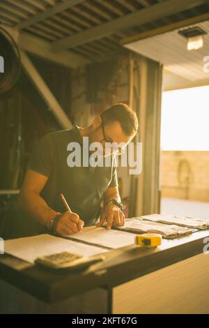 Concentrated male artisan writing on paper sheet while ordering parts at table in workshop Stock Photo