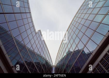 From below contemporary buildings with reflective glass walls located against gray sky on city street Stock Photo