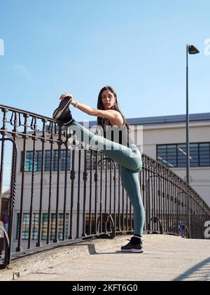 Side view of young female in sportswear leaning on railing and looking away while working out on staircase against cloudless blue sky Stock Photo