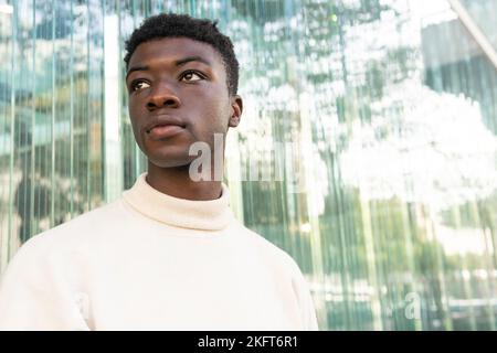Portrait of serious African American male in casual clothes looking away while leaning on glass wall Stock Photo