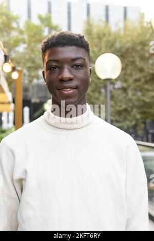 Ethnic young guy in black clothes standing on street and looking at camera friendly Stock Photo