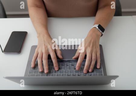 From above faceless manager in smart watch typing on keyboard of netbook while working at glass white table in office Stock Photo