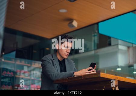 Low angle of young male using mobile phone for social media while sitting in cafe looking at screen Stock Photo