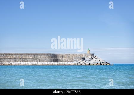 Scenic view of lighthouse located on shore of rippling sea against blue sky on sunny day in Getaria Spain Stock Photo