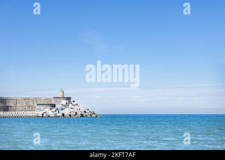 Scenic view of lighthouse located on shore of rippling sea against blue sky on sunny day in Getaria Spain Stock Photo