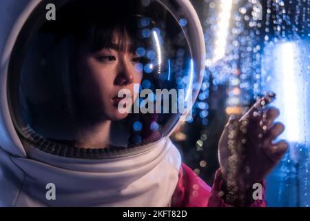 Young Asian female wearing cosmonaut helmet looking away while touching air full of bokeh lights Stock Photo