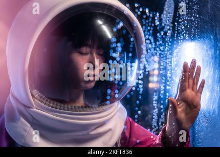 Young Asian female wearing cosmonaut helmet with closed eyes while touching air full of bokeh lights Stock Photo