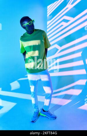 Young African American male in casual outfit posing near wall with striped shadows in bright light Stock Photo