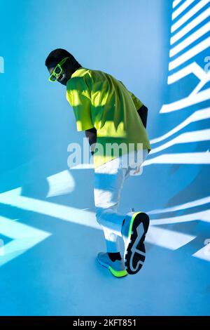 Full body of young African American male in casual outfit posing near wall with striped shadows in bright light Stock Photo
