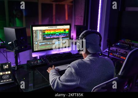 Back view of anonymous male audio engineer using computer while recording song of singer standing in studio Stock Photo