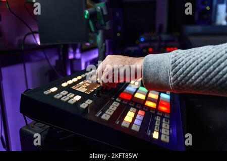 Cropped unrecognizable man sitting at workplace pushing button on mixer console while recording music in studio Stock Photo