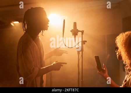Side view of African American woman using smartphone near microphone smiling and black male with singing song Stock Photo