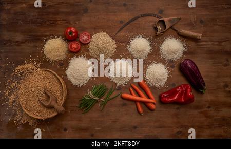 Top view of arranged small heaps of organic grains with fresh tomatoes and beans and other vegetables on wooden table near sickle and bunch of wheat Stock Photo