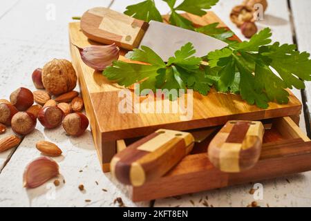 Walnuts with almonds and hazelnuts placed on wooden cutting board with parsley and garlic against knives on white wooden table Stock Photo
