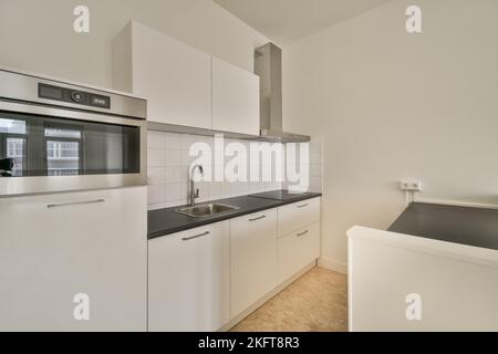 White counters with sink and appliances located against wall with built in furniture in light kitchen at home Stock Photo