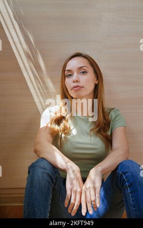 Thoughtful woman sitting on floor near wardrobe looking at camera Stock Photo