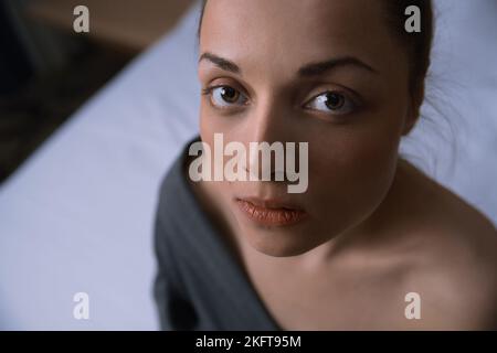 Portrait of the beautiful woman sitting on a bed and looking at camera Stock Photo