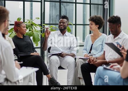 Male mentor executive leader talking during briefing, multi-ethnic workers engaged in corporate training sitting attentively listen Stock Photo