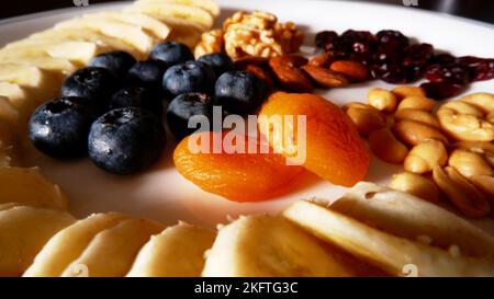 Nut with fresh and dried fruits mixed dish, blueberries, apricots snd sliced banana and shelled peanuts on the white plate. Stock Photo
