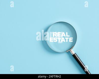 Magnifier with the text real estate on blue background. Real estate search concept. Stock Photo