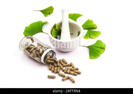 Pills and fresh green ginkgo biloba leaves, mortar and pestle on white background. Top view. Stock Photo
