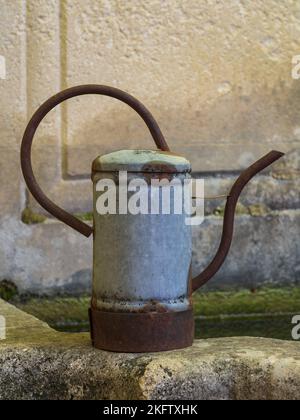 Closeup profile view of traditional vintage tin and rusted iron watering can isolated on stone fountain edge in garden Stock Photo