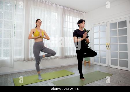 Young woman and man doing yoga with stretch muscles leg and hands at home, couple training practicing workout with yoga for bodycare, rehab with flexi Stock Photo