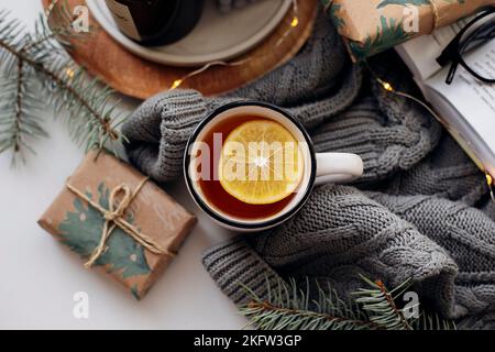 Cozy winter breakfast concept. Tea with lemon, candles, books and warm knitted sweater on white background. Top view Stock Photo