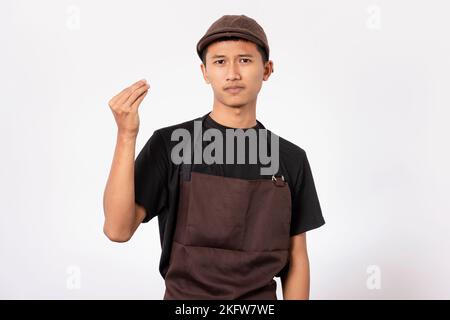 handsome barista asian man wearing brown apron and black t-shirt isolated over white background. Barista doing Italian gesture with hand and fingers. Stock Photo