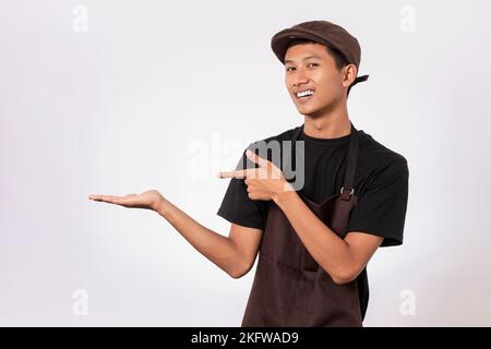 Handsome barista asian man wearing brown apron and black t-shirt isolated over white background pointing with fingers. showing product recommendation Stock Photo
