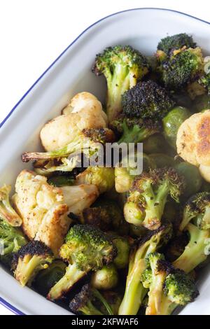 Brussels sprouts, cauliflower and broccoli, oven roasted in olive oil,  in an enamel dish bowl. Isolated on a white background Stock Photo