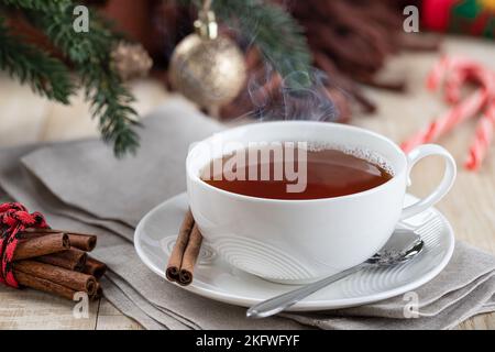 Steaming hot cup of tea on a wooden table with Christmas decorations in background Stock Photo