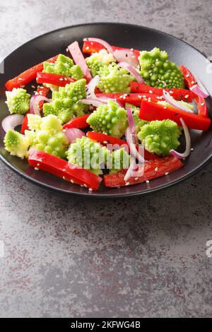 Fresh salad of steamed romanesco broccoli, bell pepper and red onion sprinkled with sesame seeds close-up in a plate on the table. Vertical Stock Photo