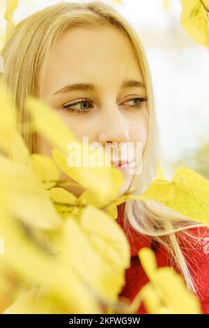 A young blonde woman walks around the autumn city in a red coat. The concept of urban style and lifestyle. Stock Photo