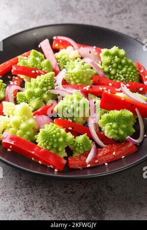 Vegetarian salad of steamed romanesco broccoli, bell pepper and red onion close-up in a plate on the table. Vertical Stock Photo