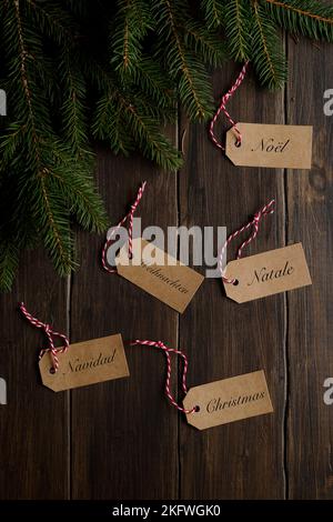 Fir branches on a wooden background, labels with Christmas written in Italian, English, French, Spanish and German. Christmas, Natale, Weihnachten, Na Stock Photo